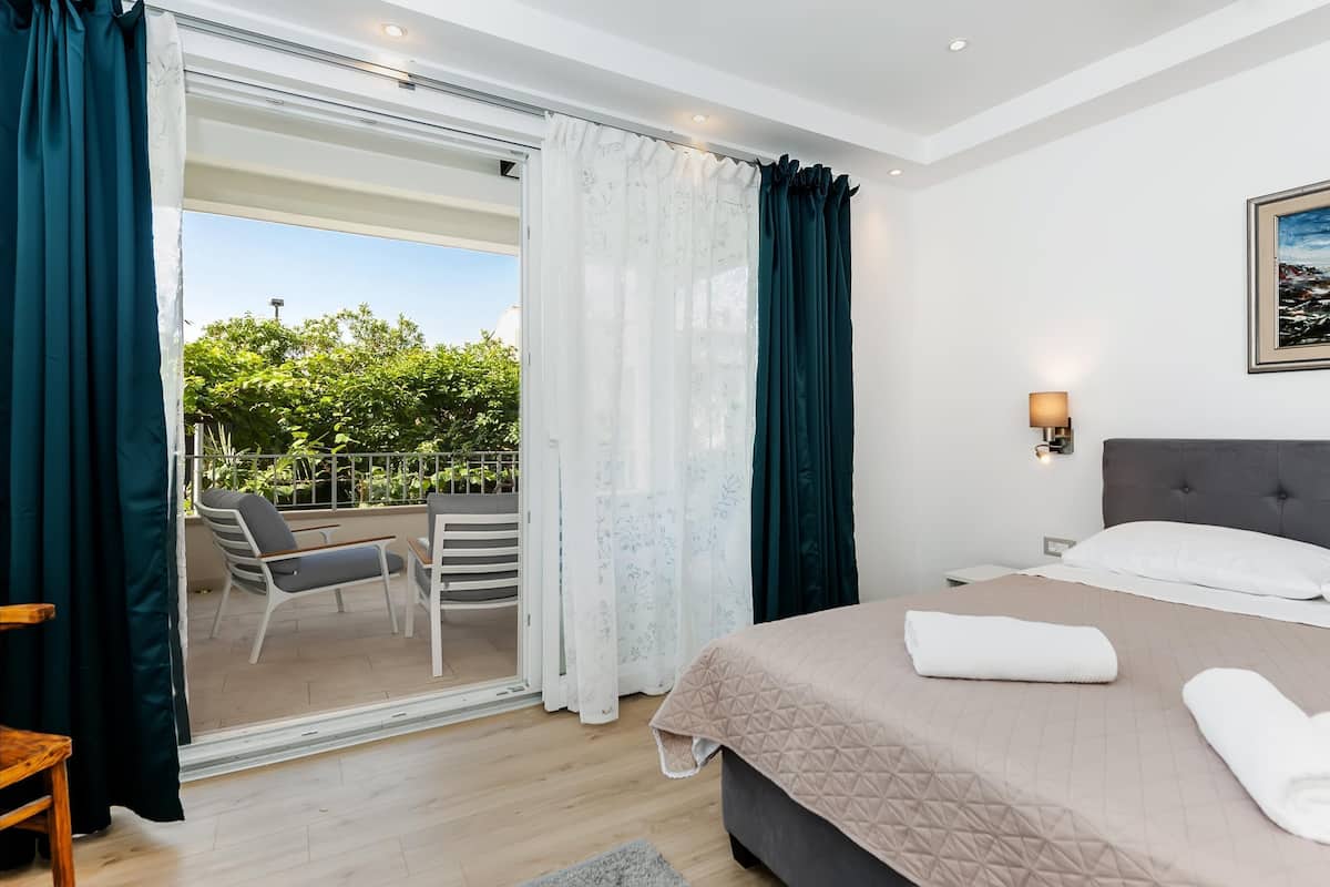 Quarto com cama, varanda com cadeiras e vista para área verde.