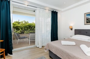A bedroom with a bed, a balcony with chairs, and a view of greenery. - Apartments El Corsaro (Rovinj)