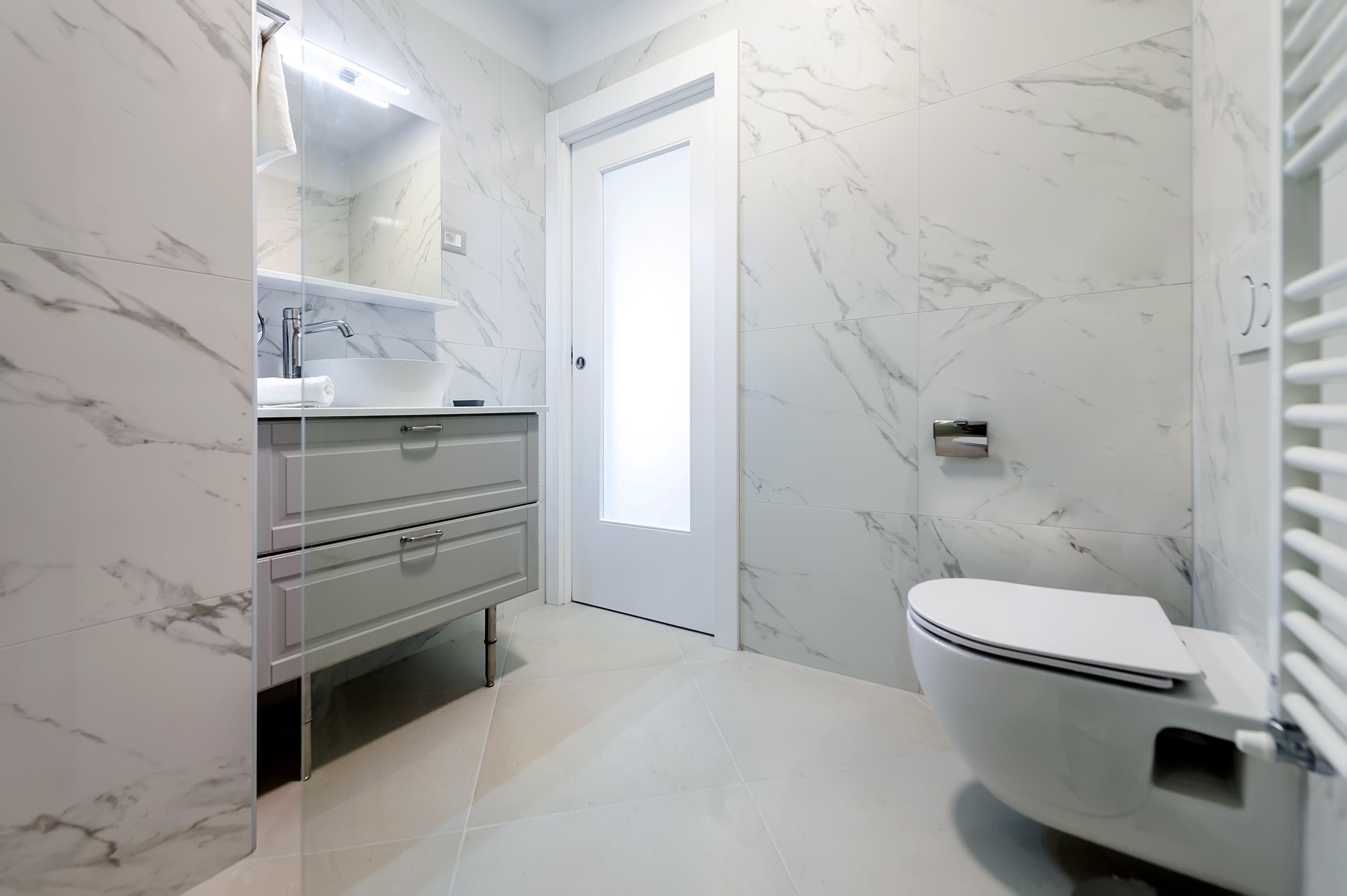 Une salle de bain moderne avec des murs en marbre, un lavabo blanc et des toilettes.