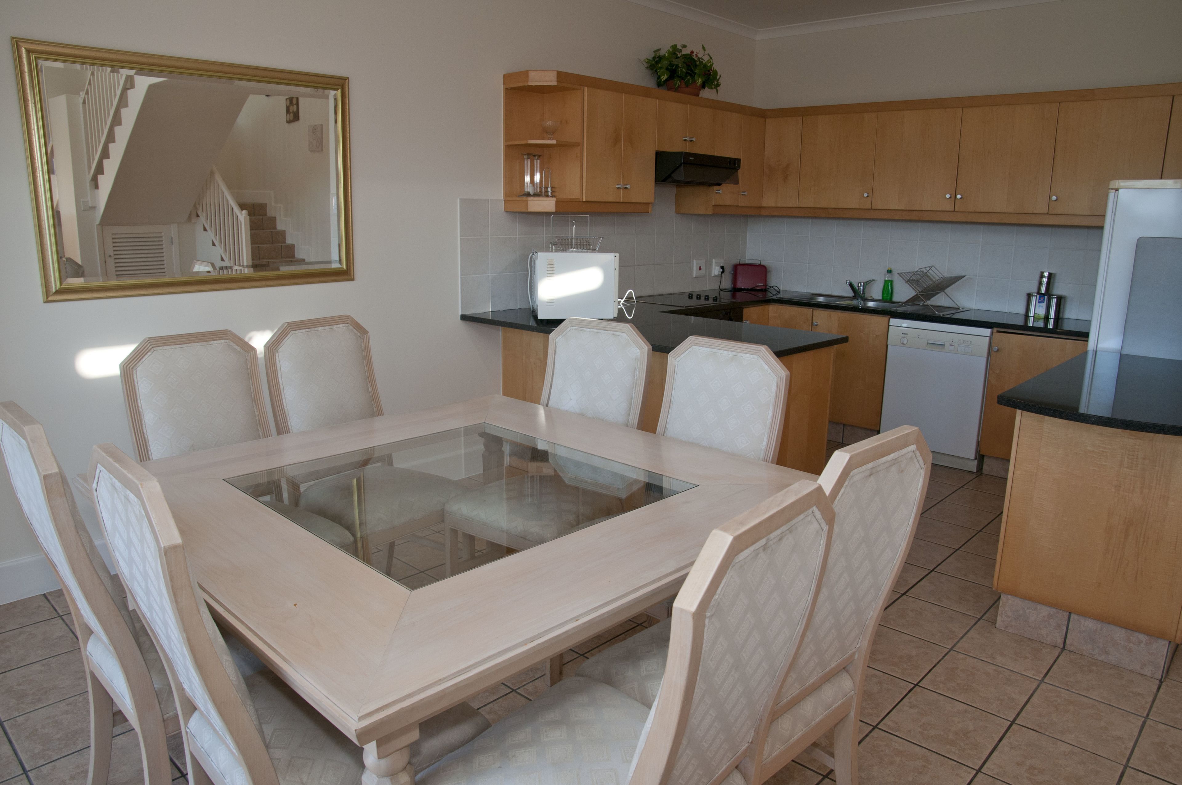 A modern kitchen with wooden cabinets, a glass-top dining table, and a built-in dishwasher.