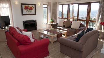 A living room with two sofas, a coffee table, a fireplace, and large windows offering a view.