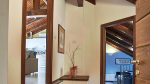 A hallway with wooden beams, a bench, and a view into a living area.