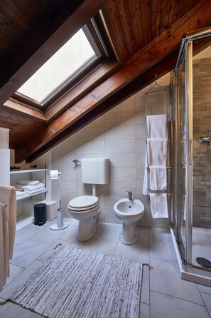 Un baño moderno con tragaluz, ducha de vidrio y suelo de baldosas blancas.