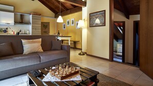 A living room with a sofa, a coffee table with a chessboard, a lamp, and a kitchen in the background.
