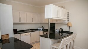 A kitchen with white cabinets, a black countertop, a stove, and a sink. - Villa 17 (Knysna)