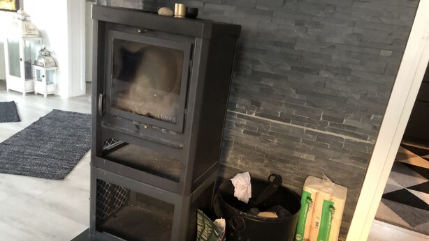 Uma sala de estar moderna com uma lareira a lenha preta, um tapete cinza e uma parede de pedra.
