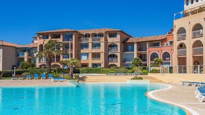 A hotel with a large swimming pool, multiple balconies, and a clear blue sky.