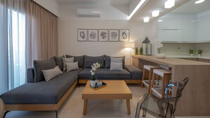 A modern living room with a grey sofa, a wooden coffee table, and a kitchen area with white cabinets. - Casa Luna Apartment,mini pool, Full Facilities (Rethymno)