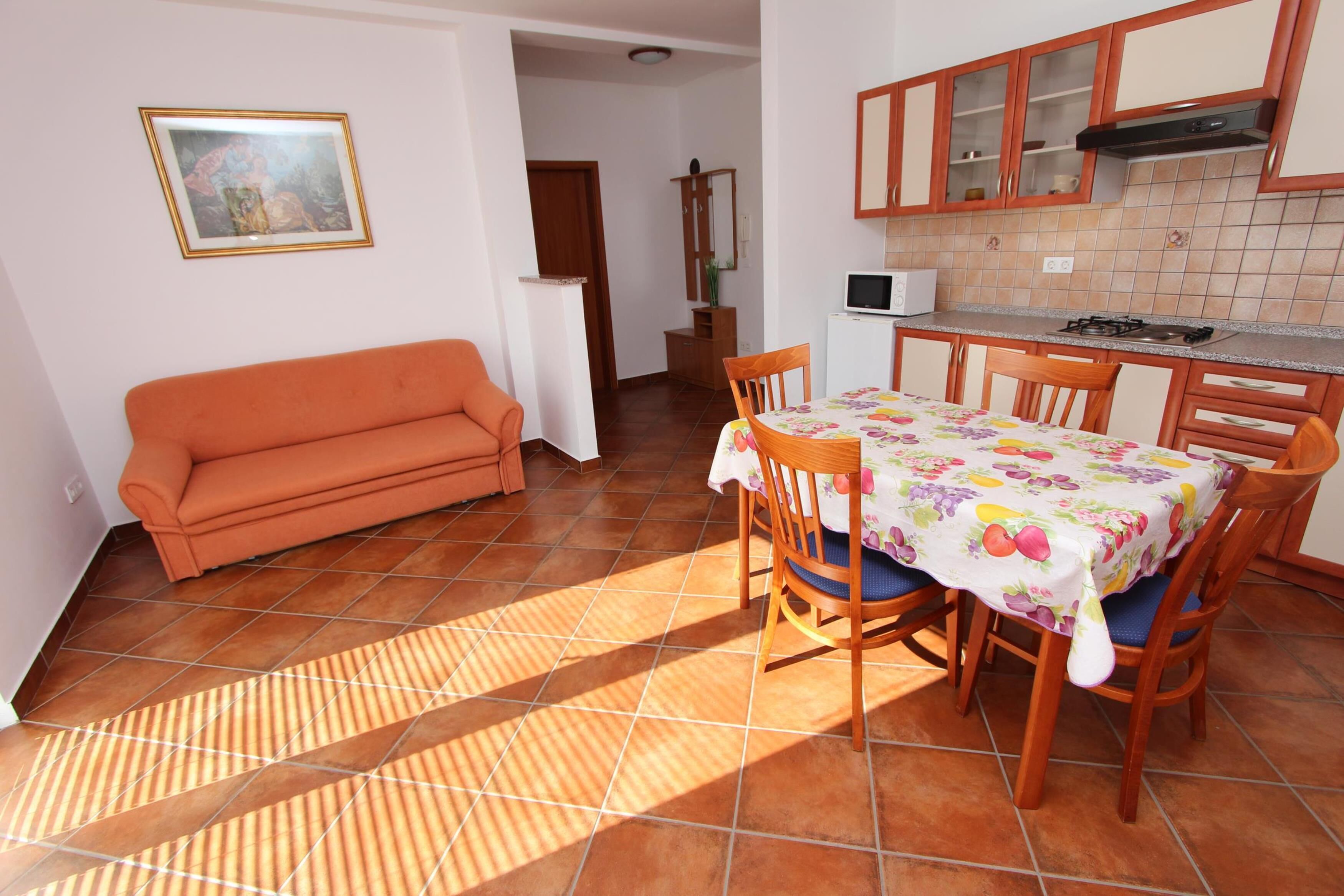 A compact living space with a sofa, dining table, chairs, and a kitchen area with cabinets and a microwave.