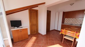 A compact kitchen with a tiled floor, wooden cabinets, a television, and a dining table with a colorful tablecloth. - Apartments Elida (Rovinj)