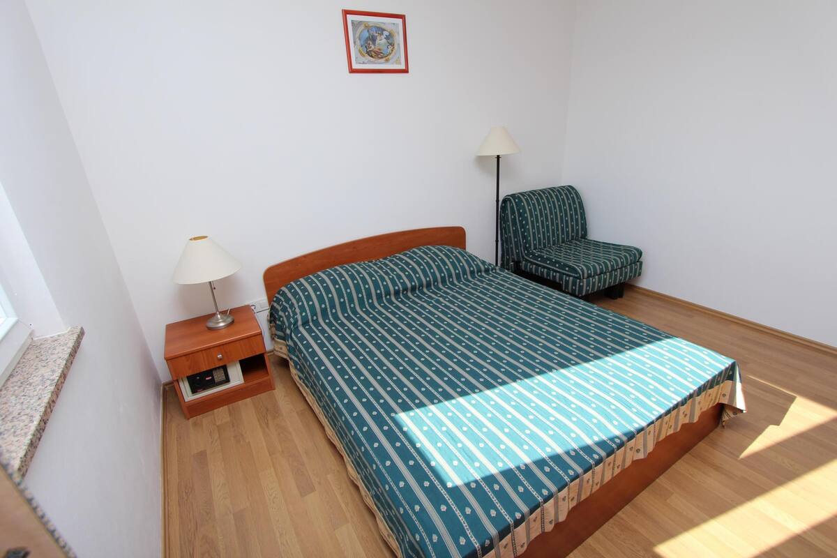 A bedroom with a bed, a chair, a nightstand, and a lamp.