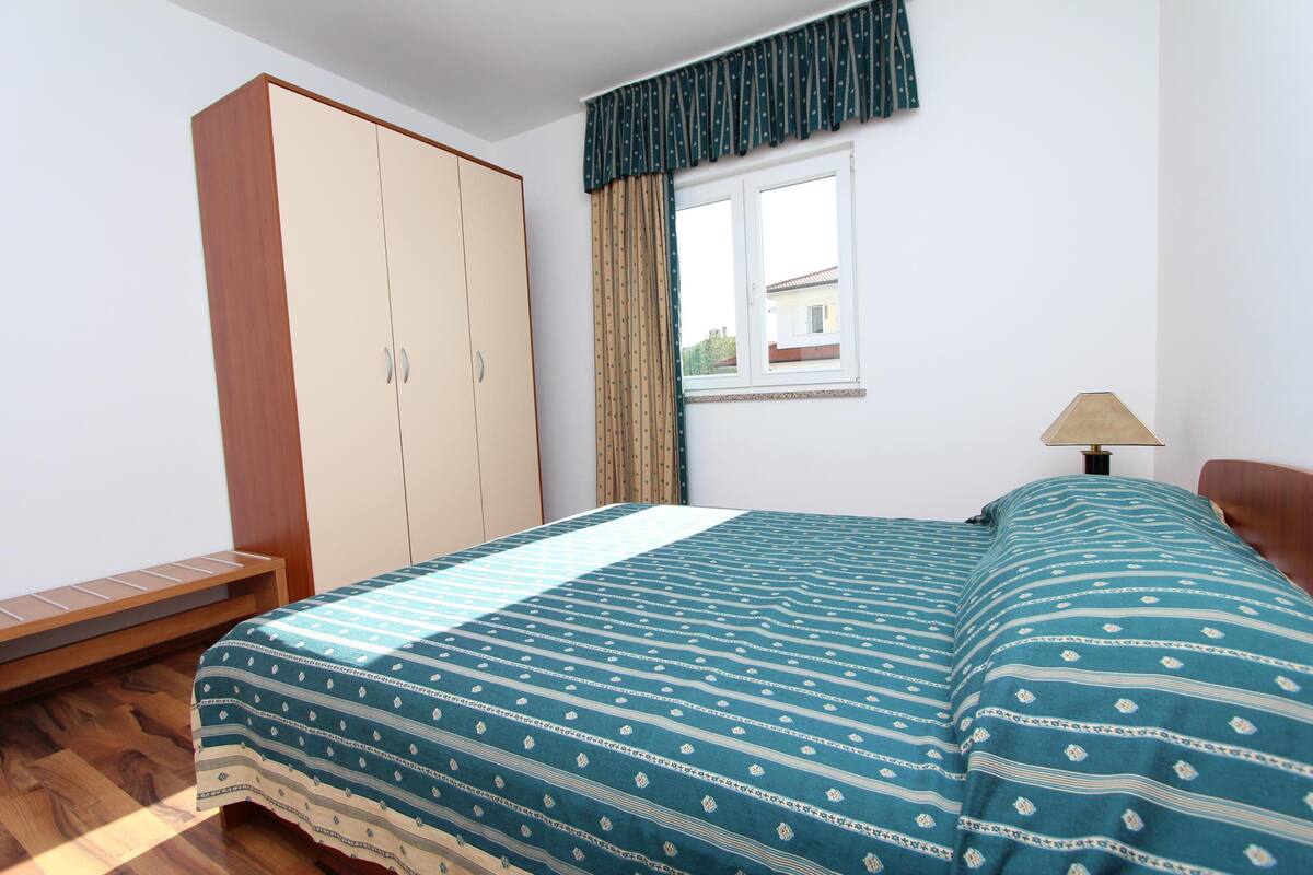 A bedroom with a bed, a wardrobe, a window with curtains, and a bedside table.