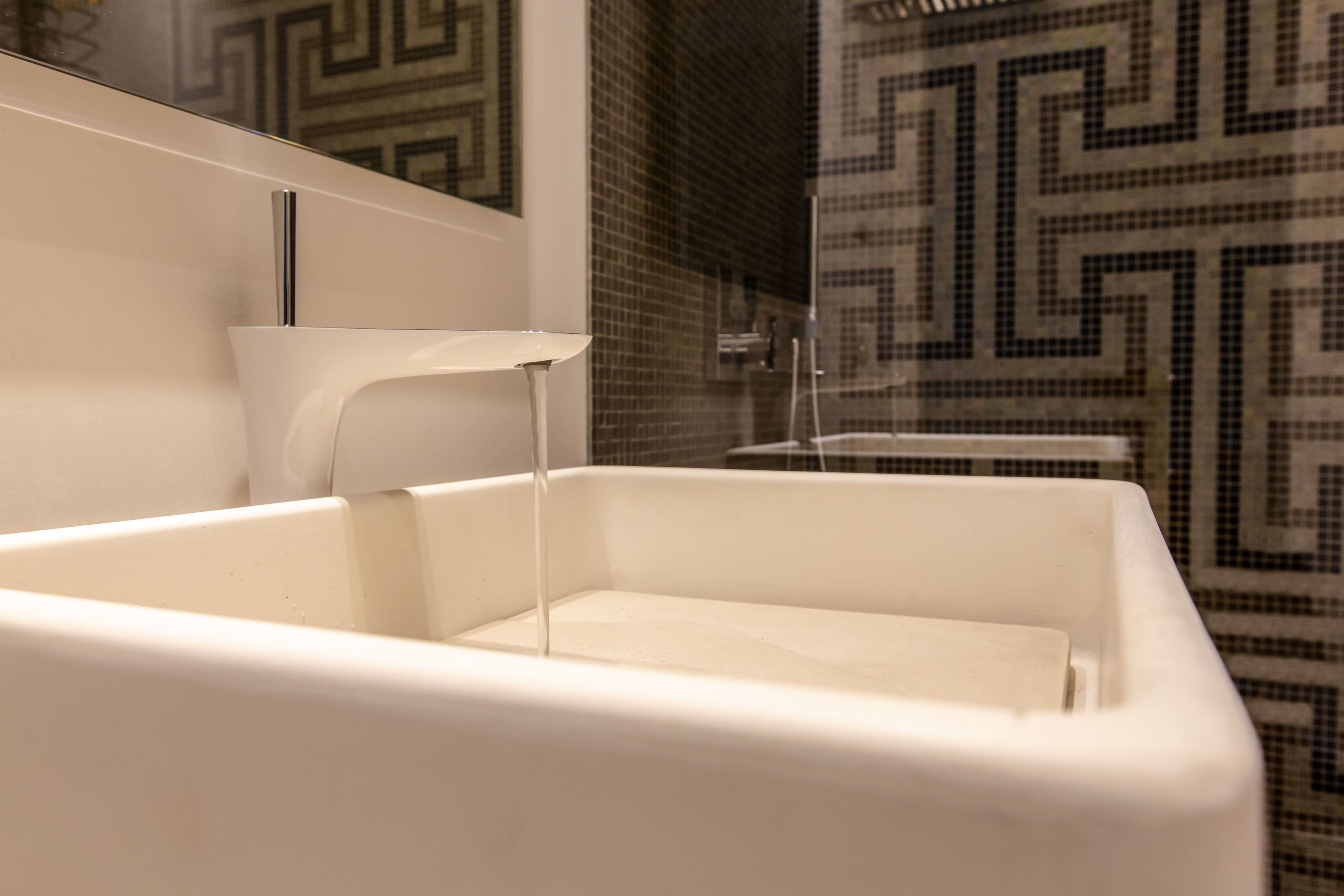 A modern bathroom with a white sink, a mirror, and a shower area with patterned tiles.