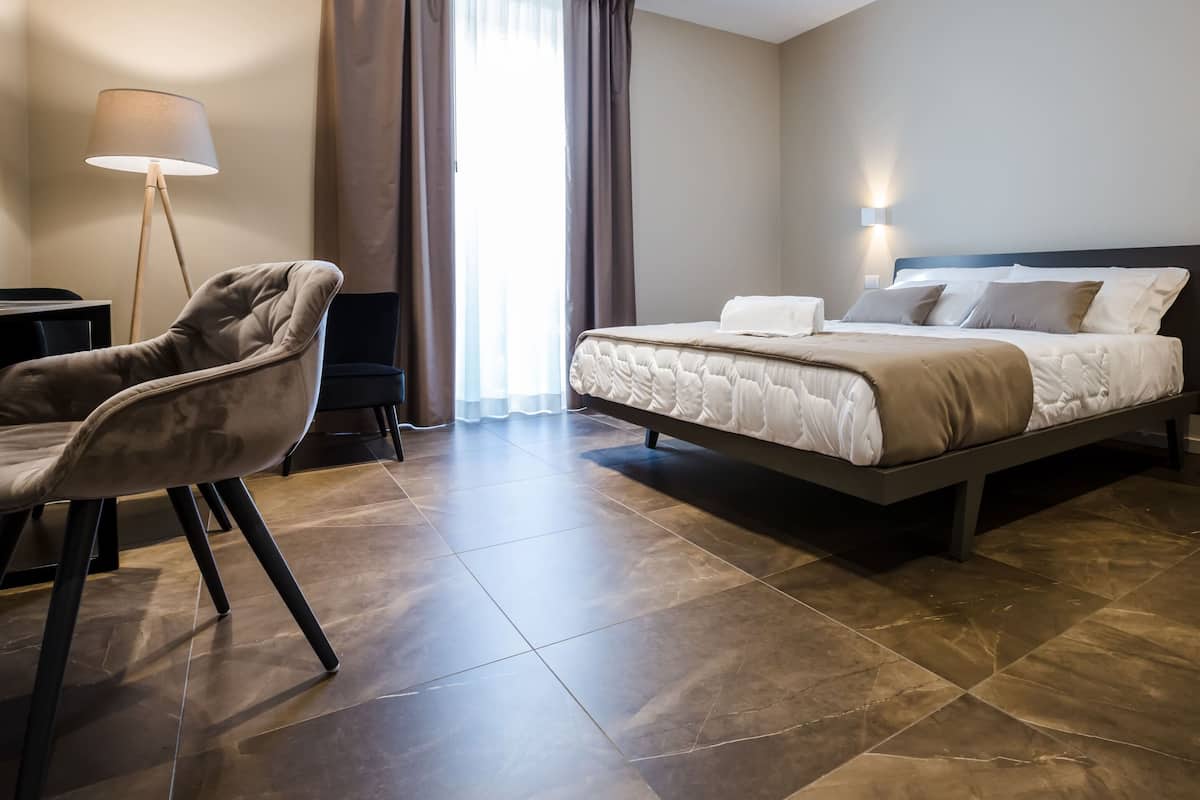 A modern hotel room with a bed, a chair, a desk, and a lamp.