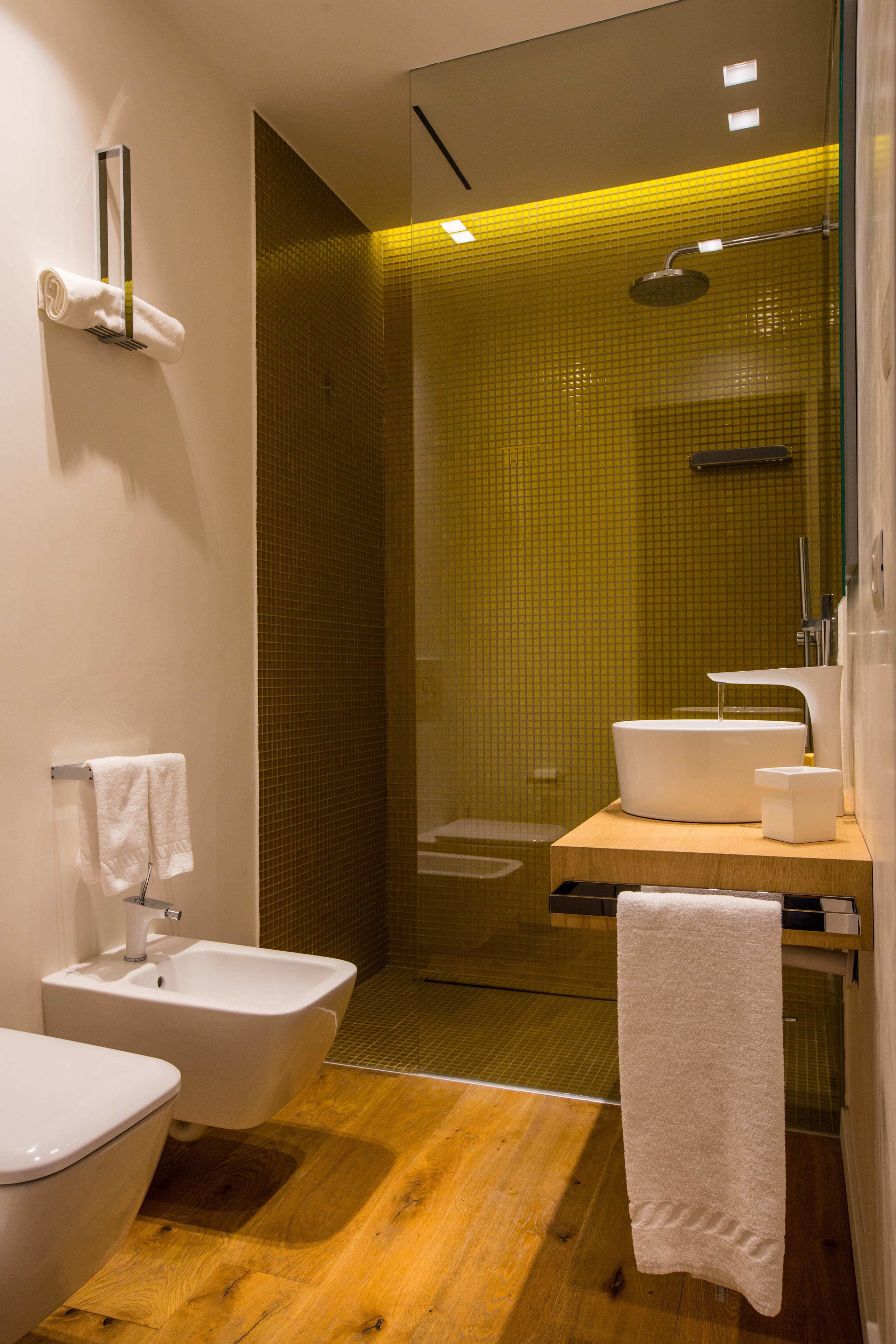 Une salle de bain moderne avec un plancher en bois, un lavabo blanc, un bidet et une douche séparée par une paroi de verre.