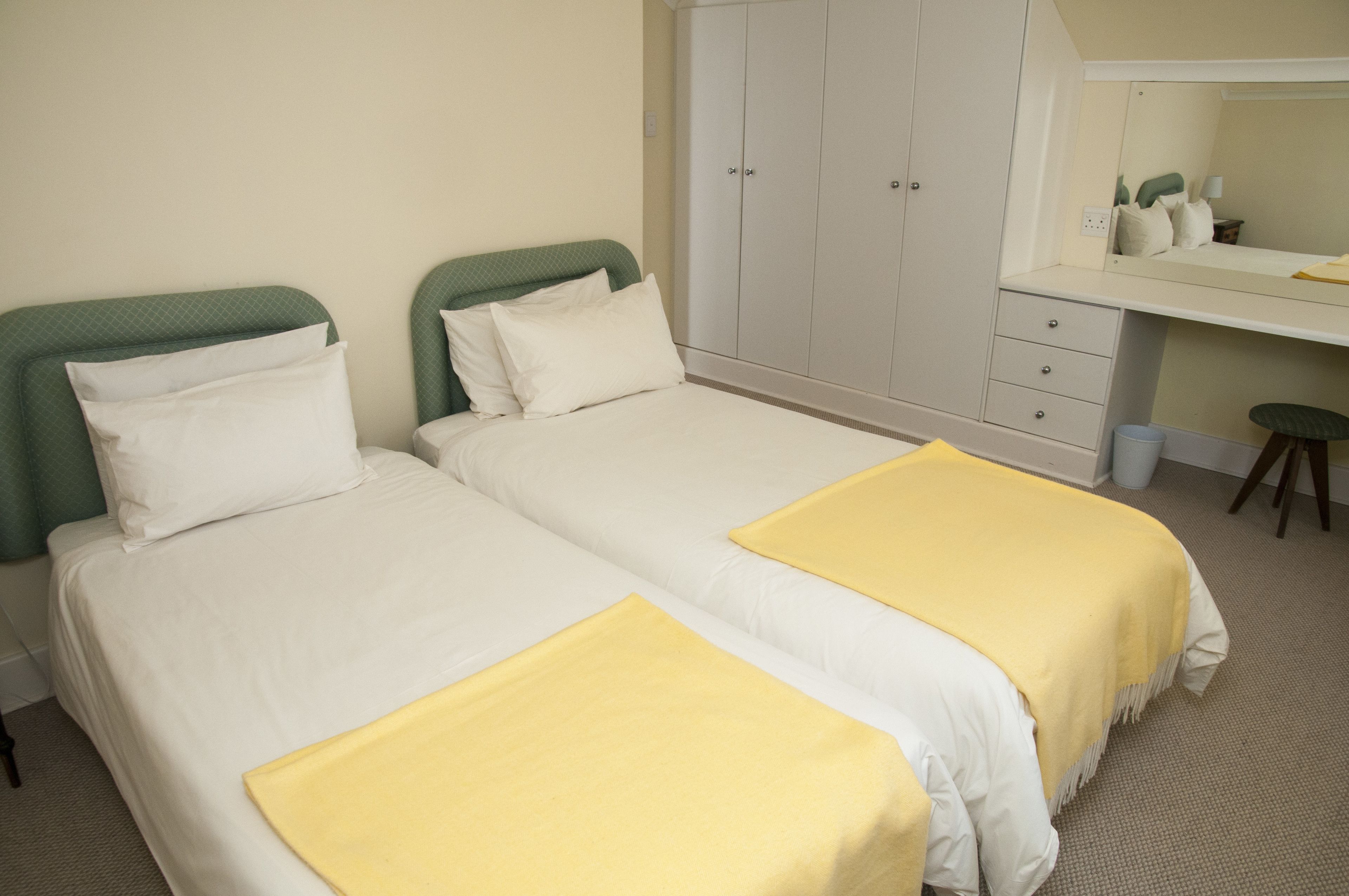 Habitación de hotel con dos camas individuales, un escritorio y un armario.
