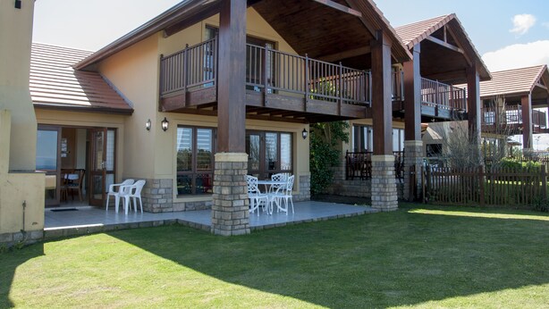A two-story house with a balcony, stone pillars, and a patio with outdoor furniture. - Villa 3 (Knysna)