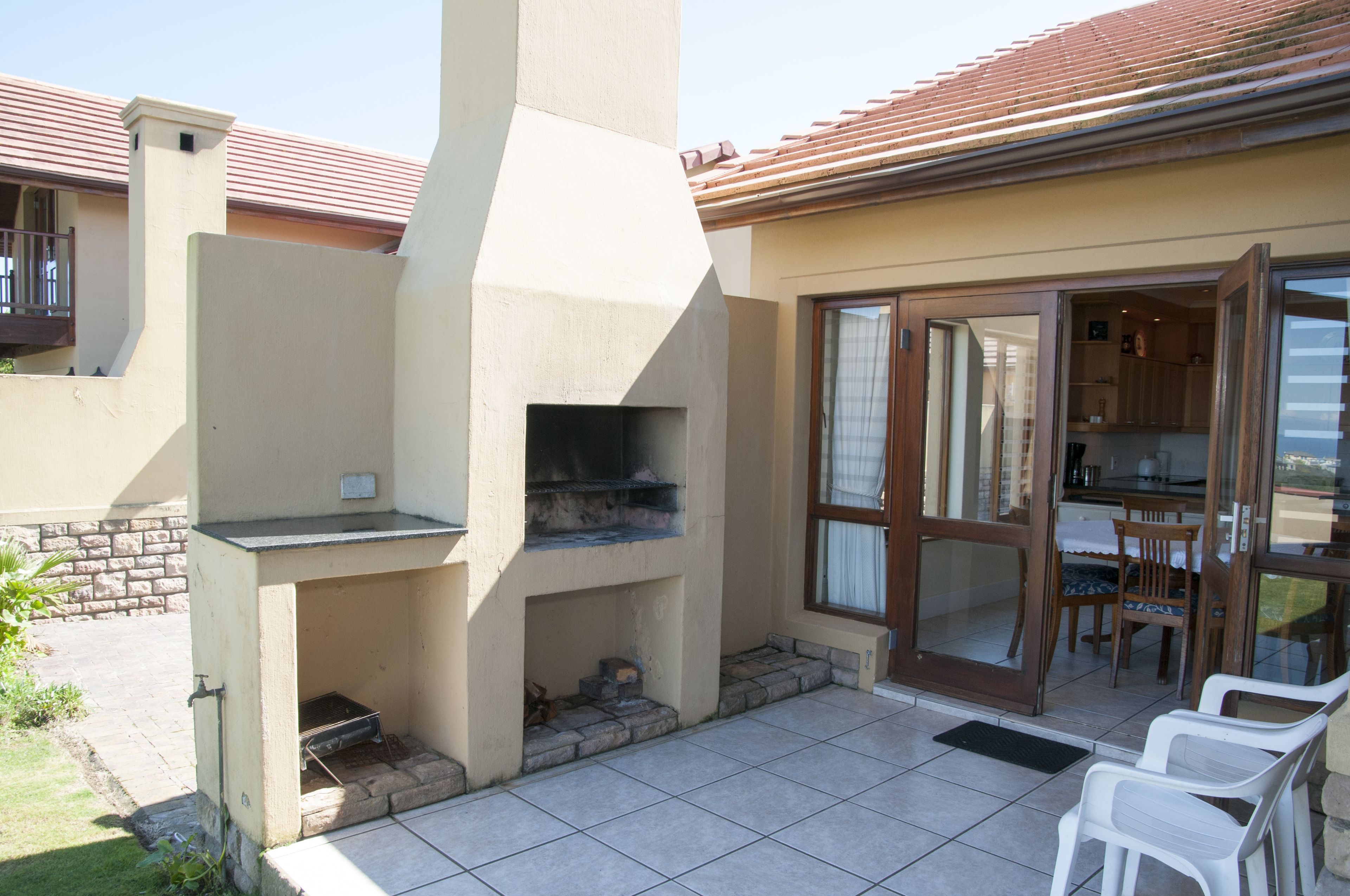 Eine Terrassengruppe mit integriertem Grill, einem Essbereich mit Stühlen und einer Glasschiebetür, die zum Küchenbereich führt.