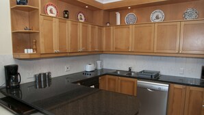 A kitchen with wooden cabinets, a granite countertop, a dishwasher, and various kitchen appliances. - Villa 3 (Knysna)