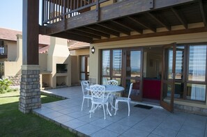 An outdoor patio with a stone pillar, white chairs, and a table.