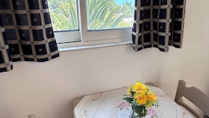 Une pièce avec une table dressée pour deux personnes, une fenêtre avec des rideaux et une vue sur la mer et les montagnes.