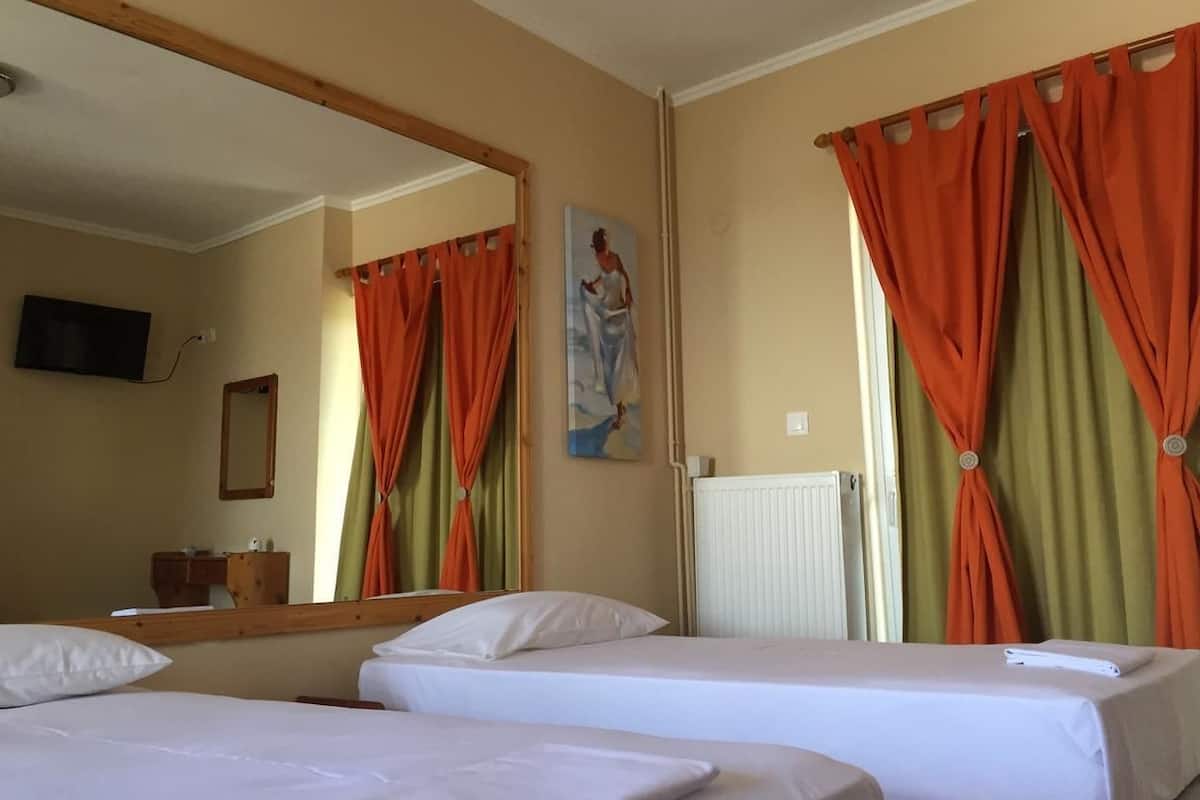 A hotel room with two beds, a large mirror, a painting on the wall, and orange curtains.