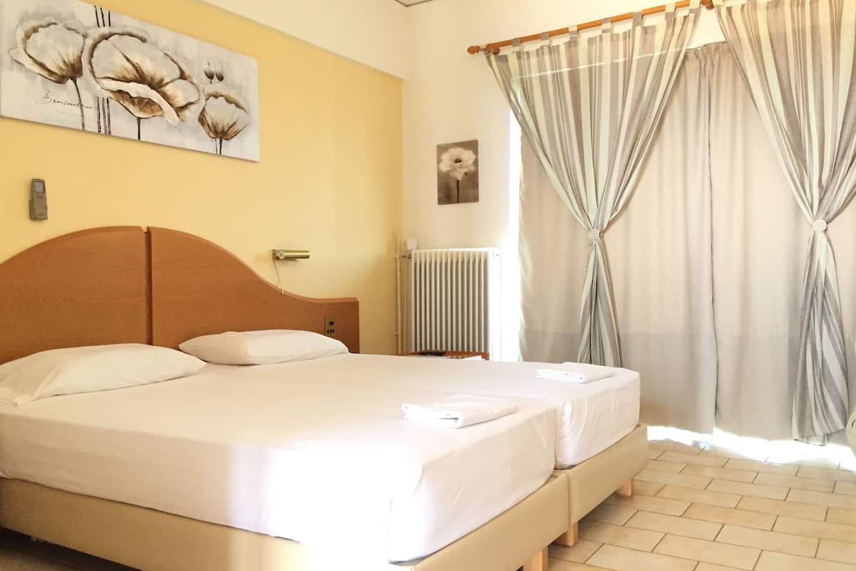 A double bed with white linens, a wooden headboard, a radiator, and a painting of flowers on the wall.