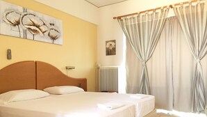 Un lit double avec du linge de lit blanc, une tête de lit en bois, un radiateur et un tableau représentant des fleurs accroché au mur.