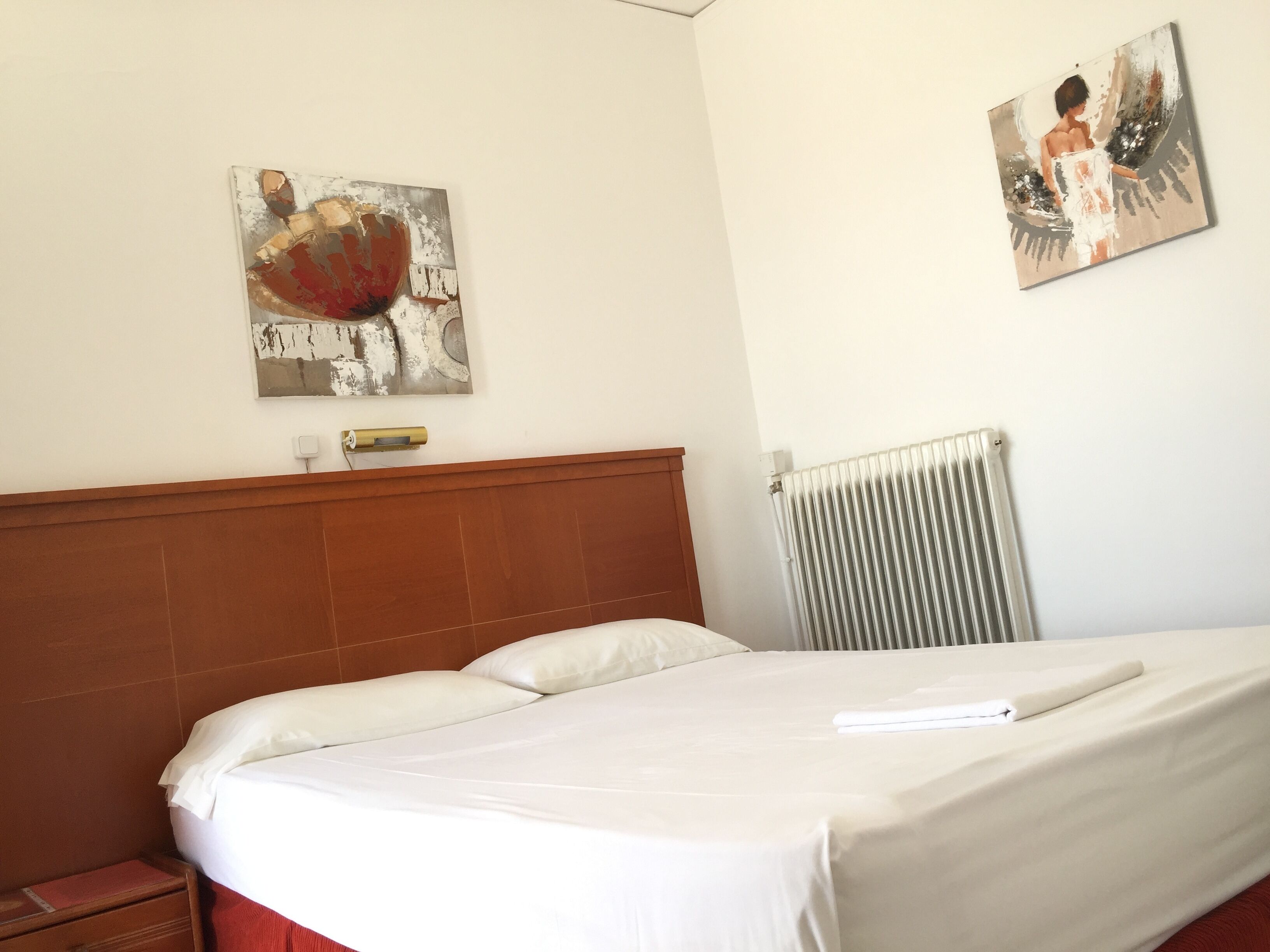 Una habitación de hotel con una cama, un radiador y dos cuadros en la pared.