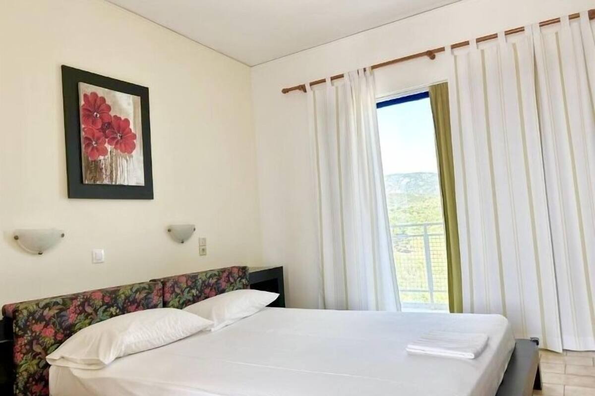 A bedroom with a bed, a floral headboard, a framed picture on the wall, and a window with curtains.