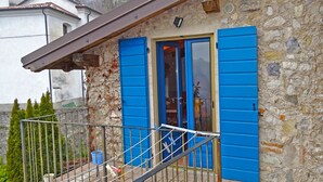 A stone building with blue shutters, a metal balcony railing, and a small blue bucket on the ground. - Rustico Colonna (Tremosine)