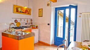 A kitchen with a gas stove, sink, and various utensils hanging on the wall. There is a blue door leading outside. - Rustico Colonna (Tremosine)