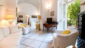 Un salon spacieux, meublé de blanc, avec une cheminée et une grande fenêtre donnant sur un paysage verdoyant.