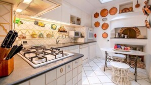 Une cuisine compacte équipée d’une cuisinière à gaz, de meubles blancs, d’un four à micro-ondes et d’un petit coin repas avec une table et des chaises blanches.