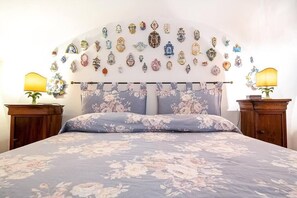 A bedroom with a floral bedspread, a headboard with decorative items, and two bedside lamps. - ORANGE HOUSE AMALFI CENTER (Amalfi)