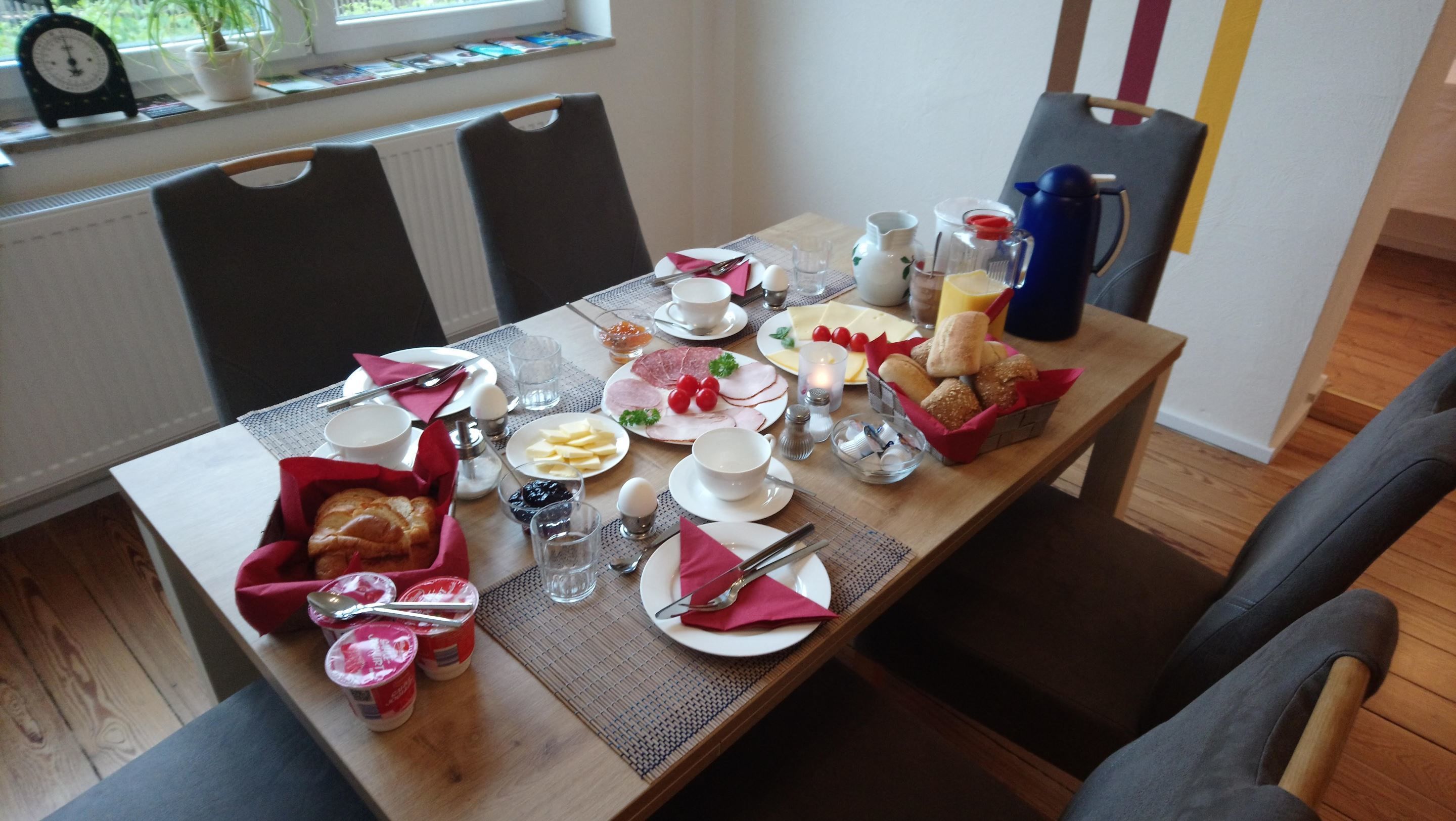 Una mesa de desayuno dispuesta con platos, cubiertos y diversos alimentos.