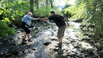 Dos personas cruzando un arroyo pedregoso en un área boscosa.