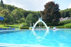 Une piscine dotée d’une structure arquée blanche au centre, entourée d’une végétation luxuriante et d’arbres.