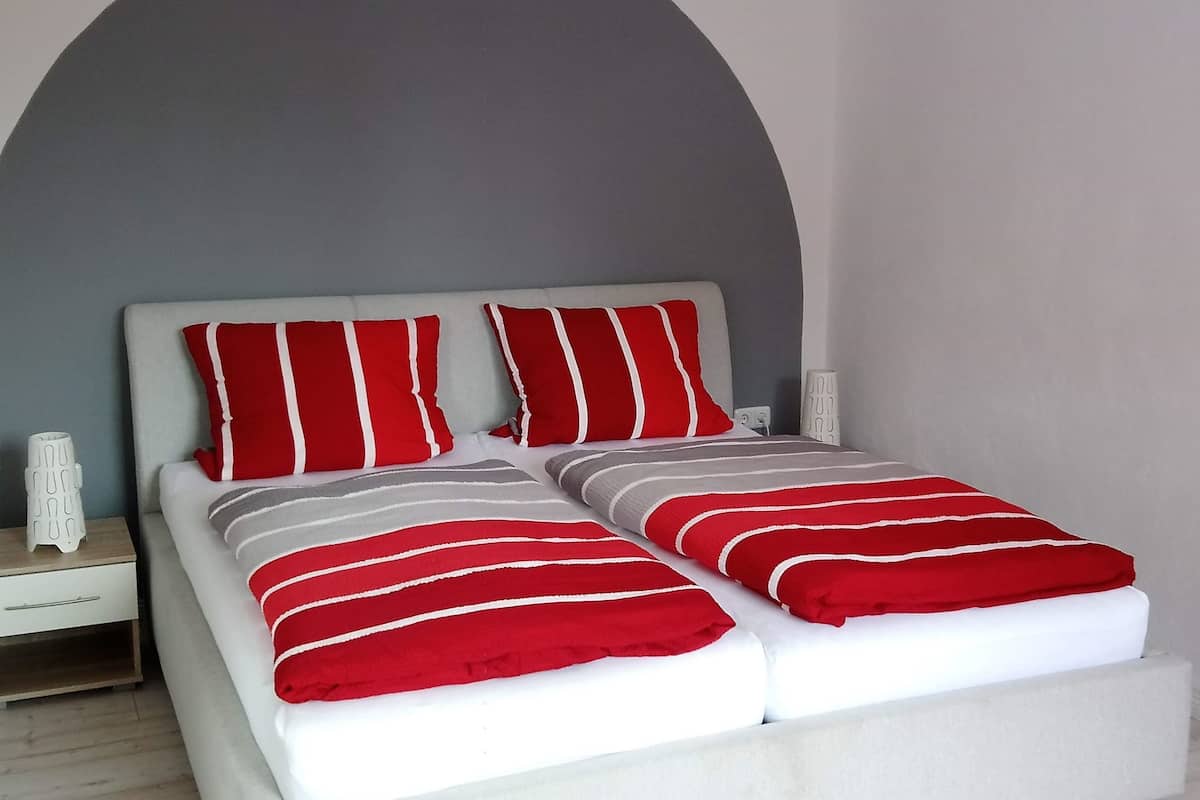 A bed with white and red striped bedding, a white nightstand, and a white lamp.