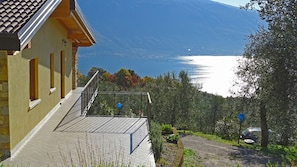 A house with a balcony overlooking a lake, surrounded by trees and a parked car.