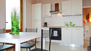 A modern kitchen with white cabinets, a built-in oven, and a coffee maker. There is a dining table with chairs and a vase of green plants. - Villa Vagne Holideal (Tremosine)