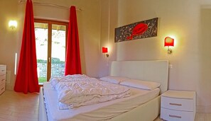 A bedroom with a bed, a nightstand, a window with curtains, and wall-mounted lights.