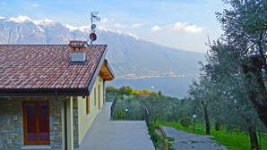 A house with a tiled roof, a stone wall, and a view of a lake and mountains. - Villa Vagne Holideal (Tremosine)
