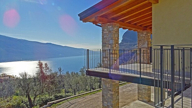 A balcony with stone pillars and a wooden roof overlooking a lake and mountains. - Villa Vagne Holideal (Tremosine)