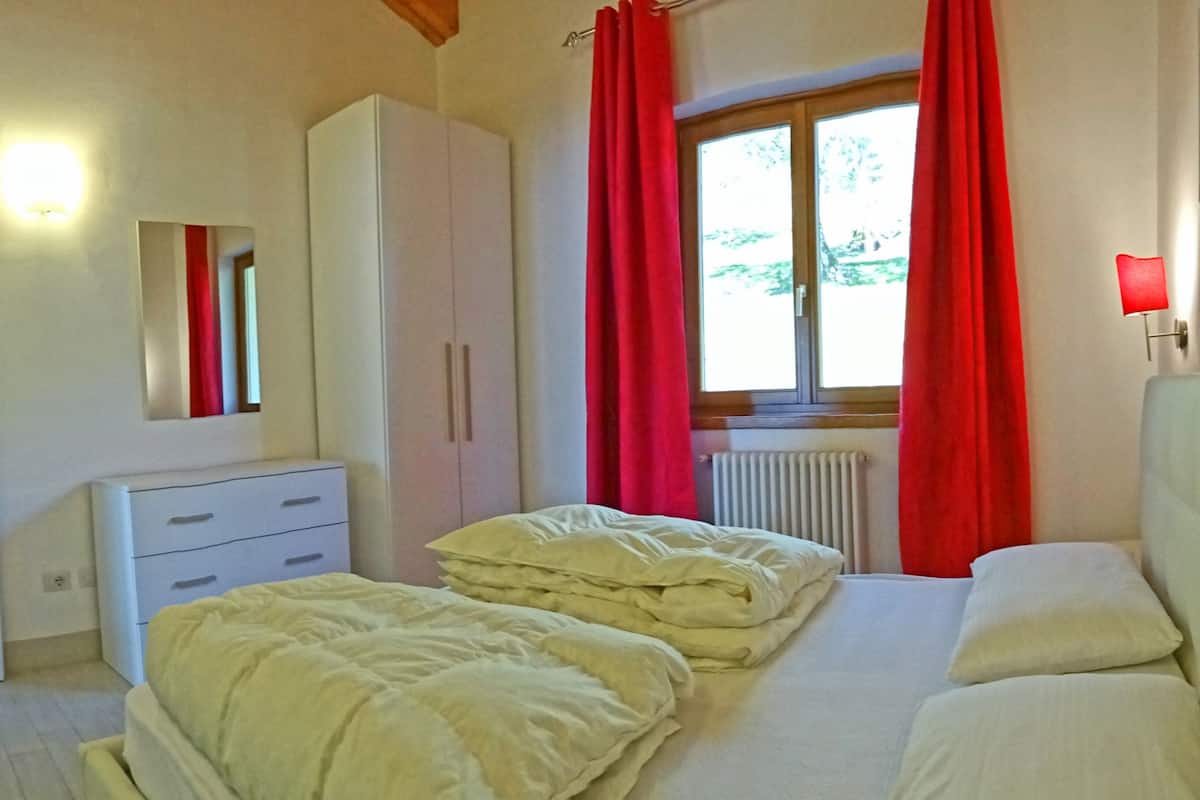A bedroom with a bed, a dresser, a mirror, and a window with red curtains.