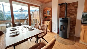A cozy dining area with a wooden table set for four, a stone wall, and a modern kitchen with a built-in oven. - Haus Sonnwiese Ski-to-Door (Bad Kleinkirchheim)