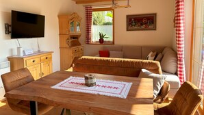 A cozy room with a wooden ceiling, a TV mounted on the wall, a wooden cabinet, a sofa, and a dining table with a placemat. - Haus Sonnwiese Ski-to-Door (Bad Kleinkirchheim)