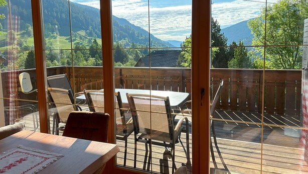A sunlit patio with a table and chairs, overlooking a mountainous landscape. - Haus Sonnwiese Ski-to-Door (Bad Kleinkirchheim)