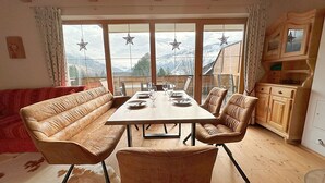 A dining area with a wooden table, leather sofas, and a view of mountains through large windows. - Haus Sonnwiese Ski-to-Door (Bad Kleinkirchheim)