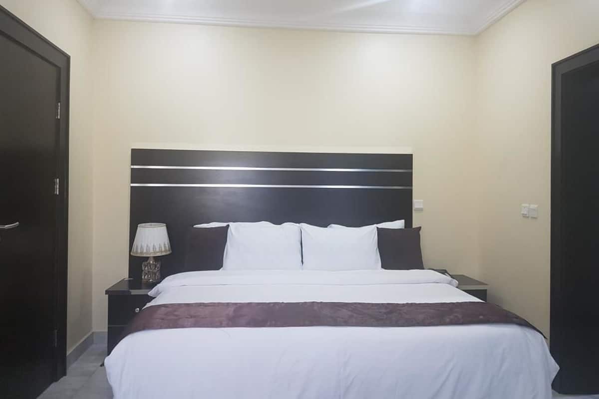 Quarto de hotel com uma cama grande, mesa de cabeceira com abajur e um guarda-roupa de cor escura.